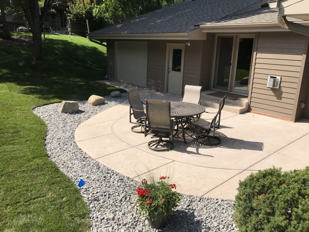 Concrete patio with outdoor dining area and gravel landscaping in a residential backyard.